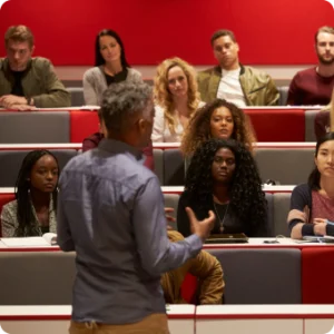 A man stands at a podium, delivering a lecture to an attentive audience in a spacious lecture hall.