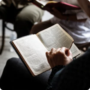 A person seated in a church, reading the Bible with focused attention, surrounded by wooden pews and soft lighting.