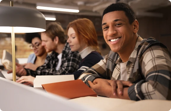 A group of students seated around a table, engaged in discussion and collaboration on their work.