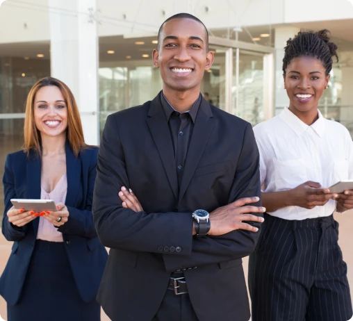 A diverse group of people stands together in front of a large building, smiling and engaging with one another.