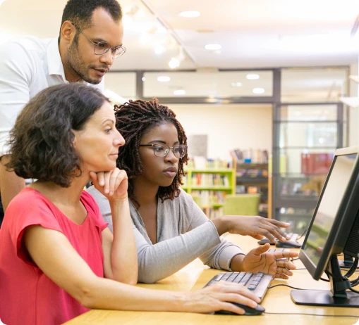 A diverse group of individuals gathered around a computer, engaged in discussion and observing the screen together.